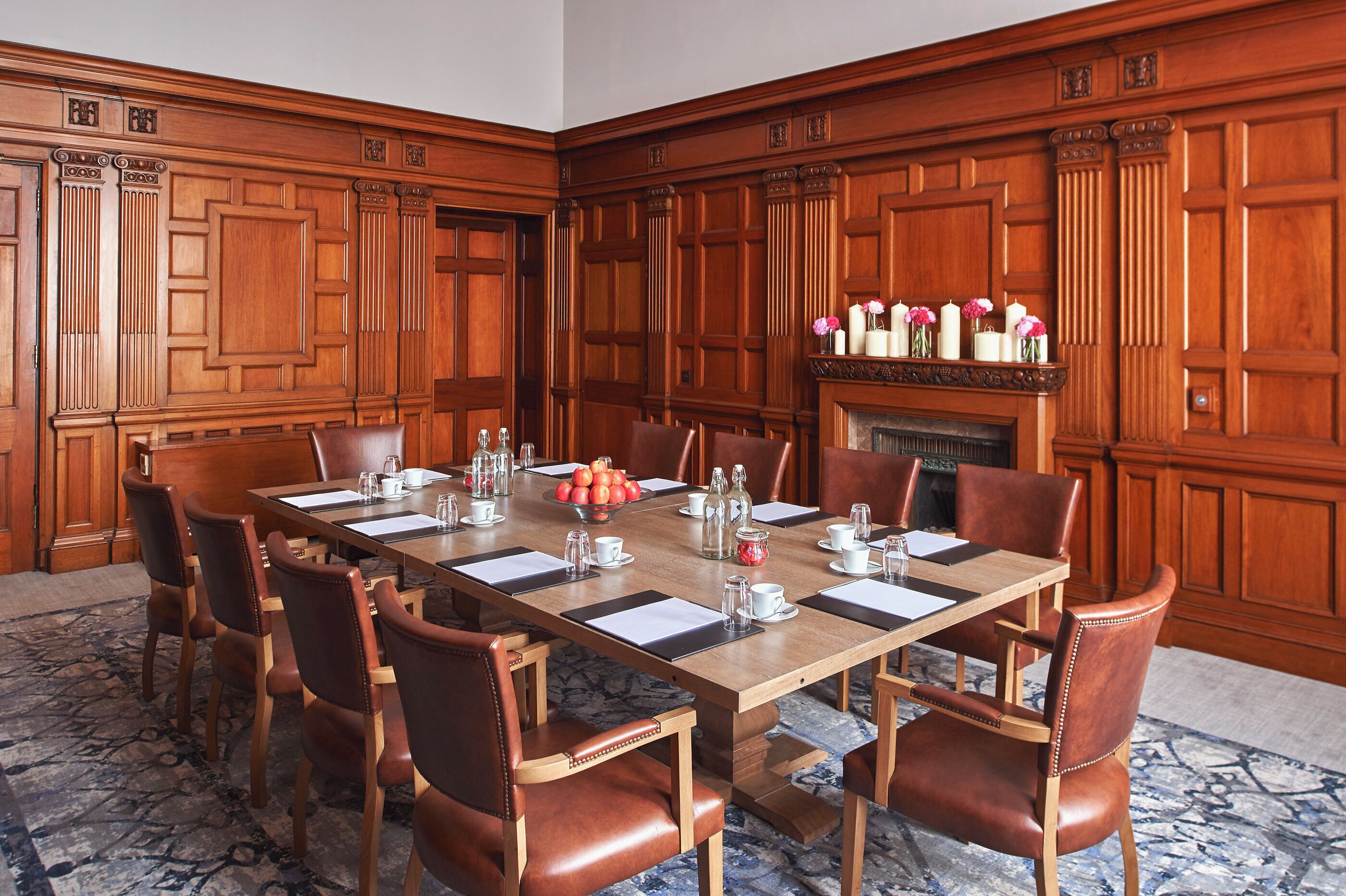 A conference room with a long wooden table, leather chairs, and a fireplace with decorative vases.