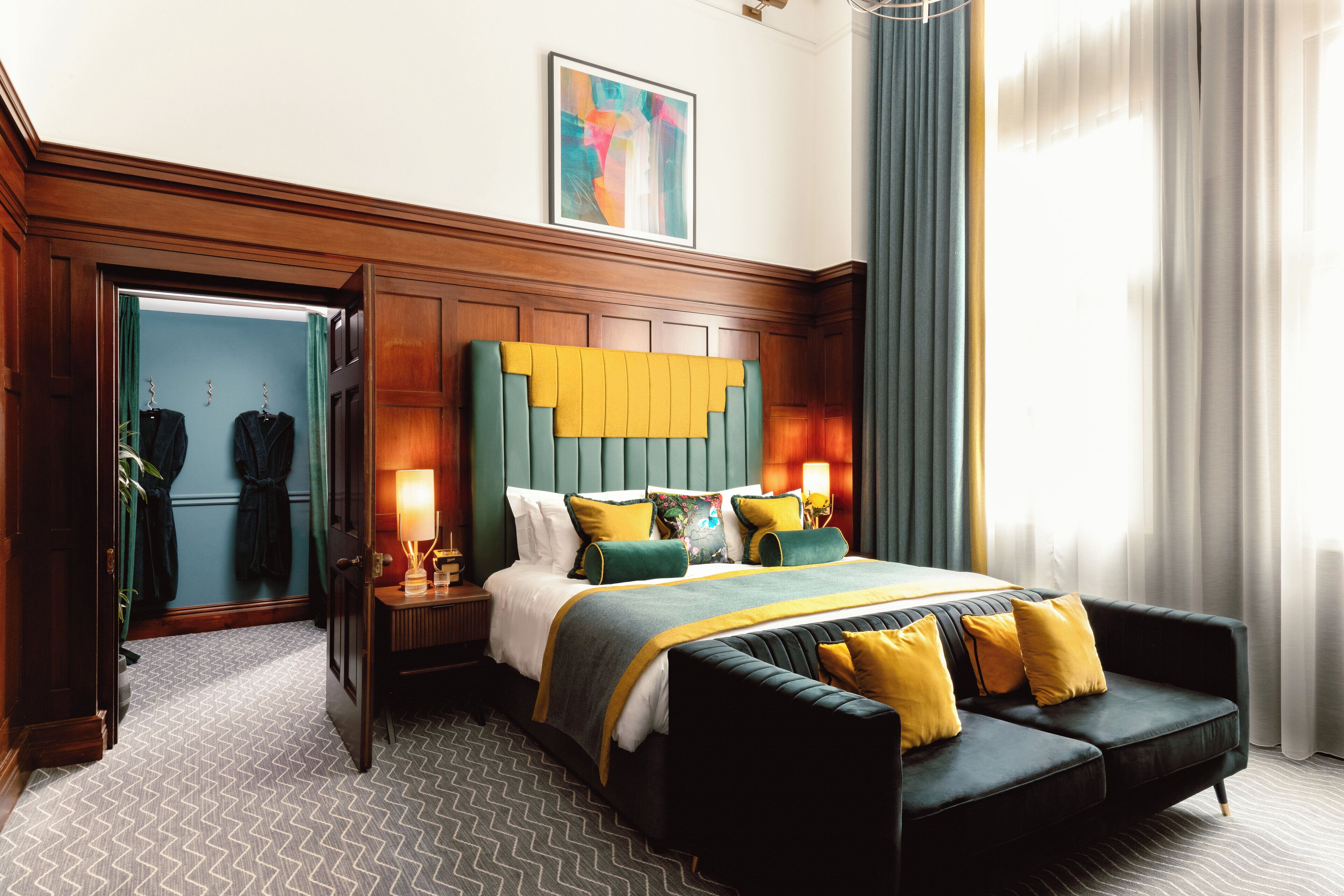 A hotel room with a large bed, a sofa, a mirror, and a painting on the wall.