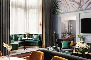 A modern living room with a green sofa, a black sofa, and a yellow armchair. There is a round table with a vase of flowers.