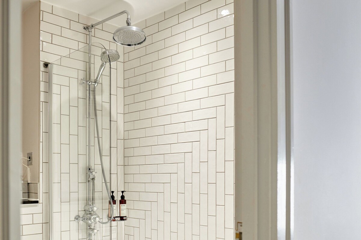 A modern bathroom with white herringbone-patterned tiles, a glass-enclosed shower, and a white bathtub.