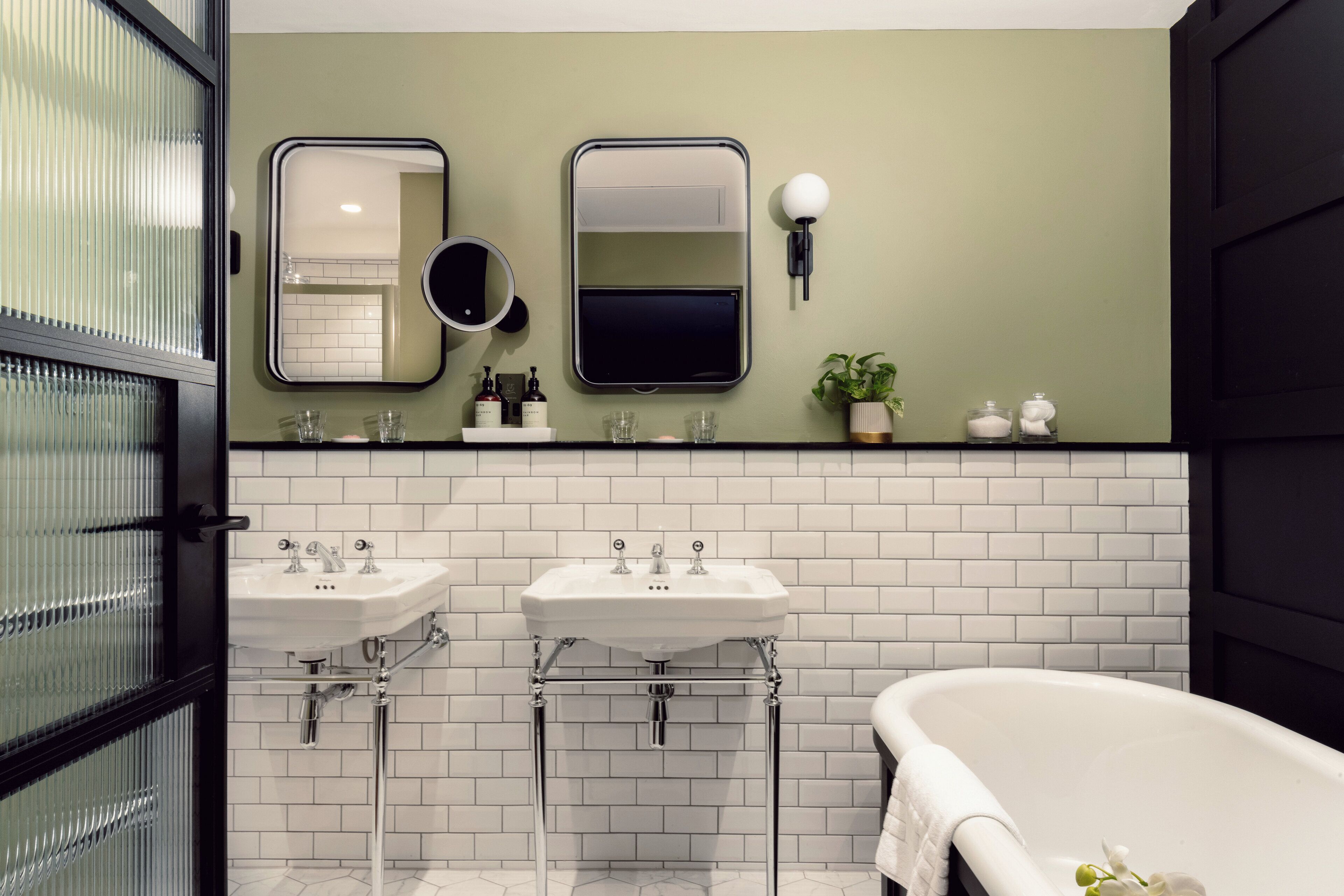 A bathroom with two sinks, a large mirror, a wall-mounted light, and a bathtub.