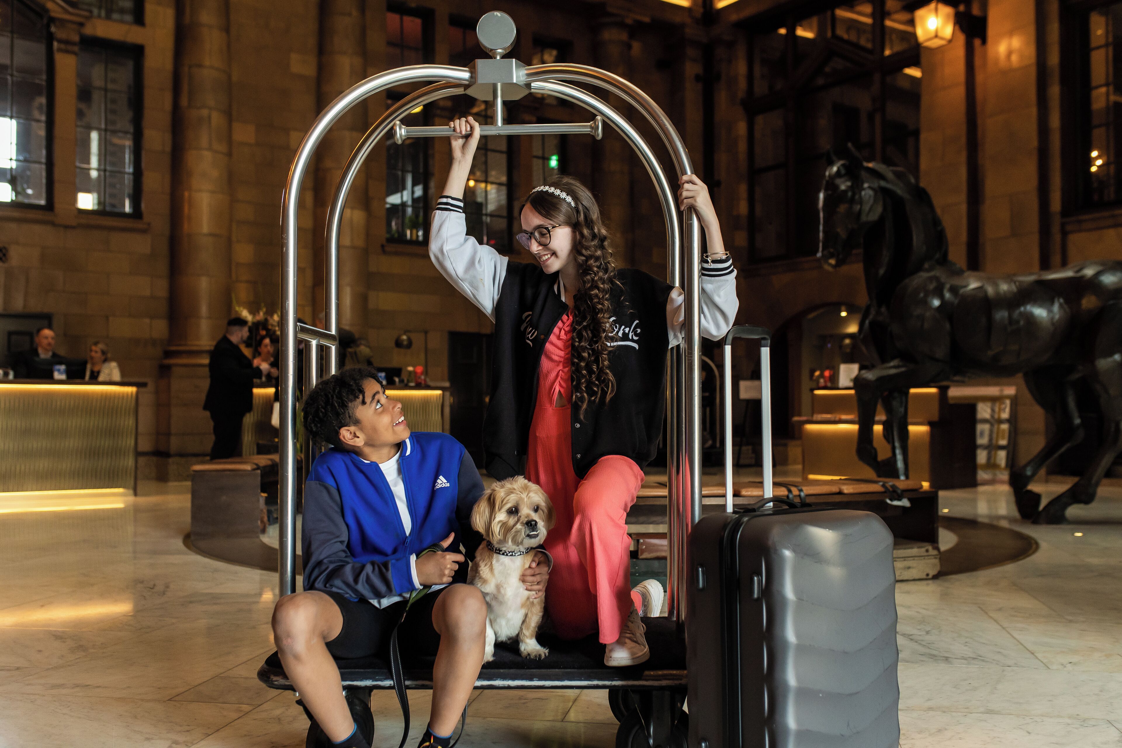 A man and a woman sitting on a lift in a lobby with a horse statue in the background.