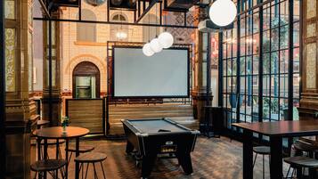 A billiards room with a pool table, stools, and a large screen.