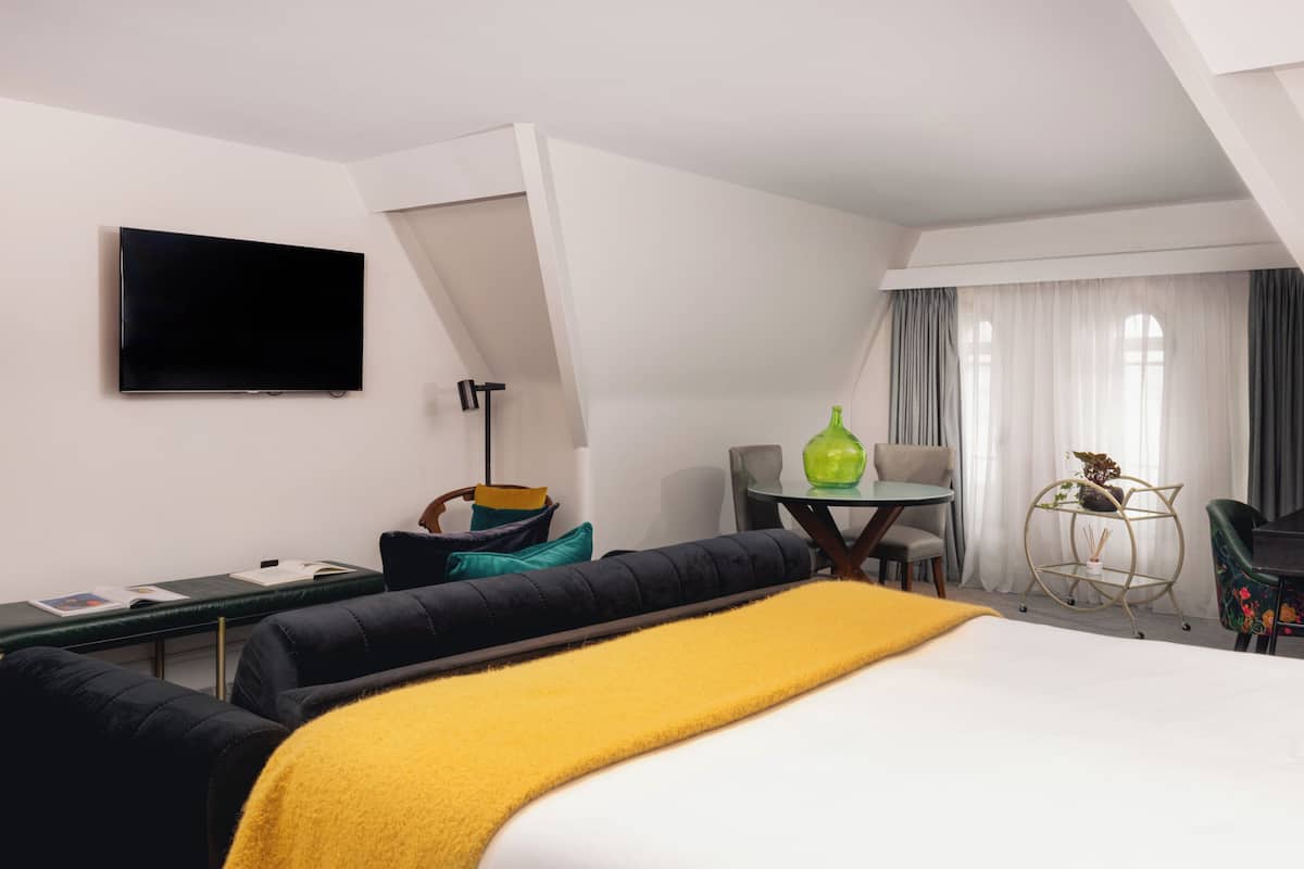 A hotel room with a bed, a desk, a chair, a TV, and a small table with a vase.