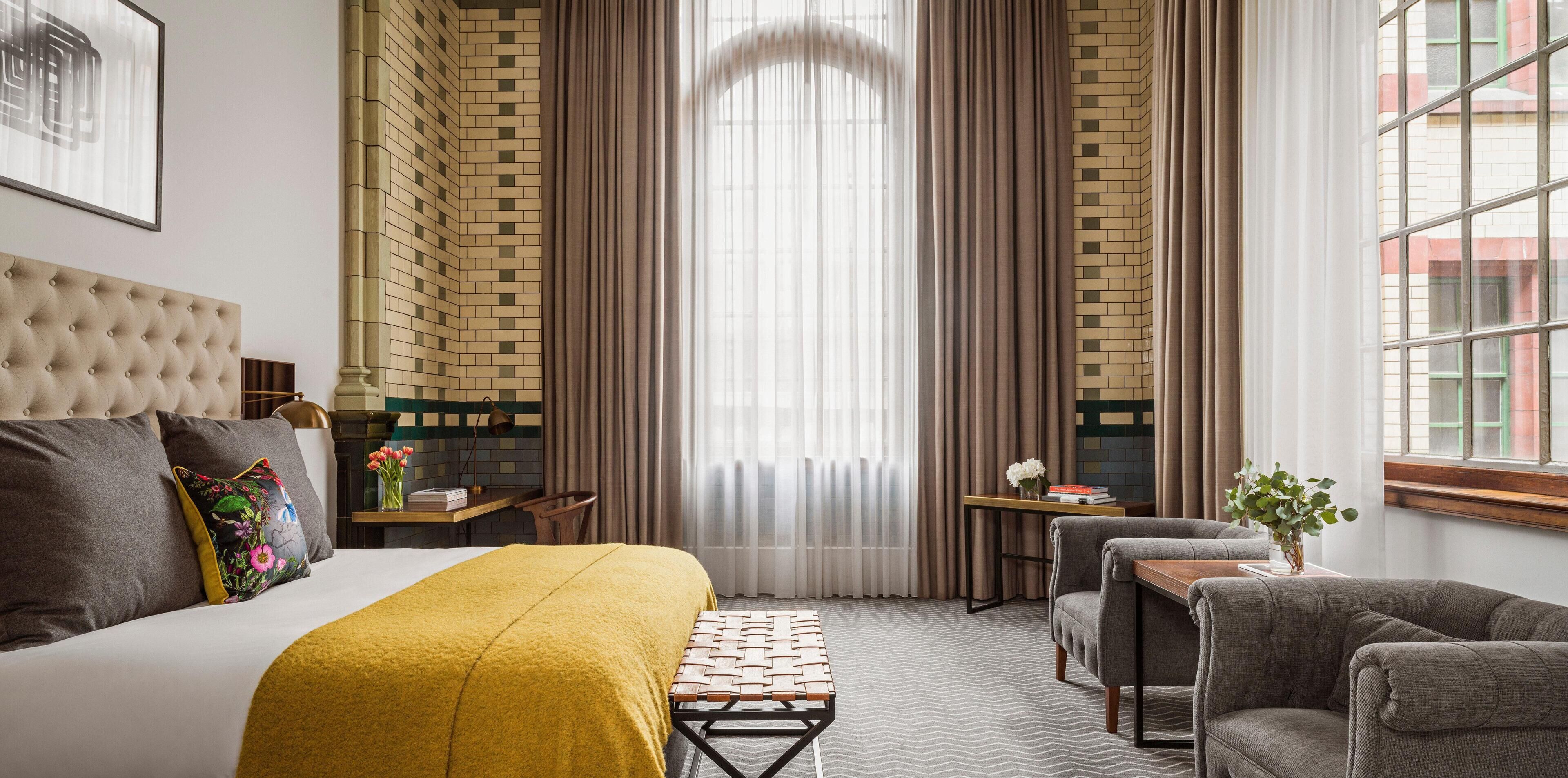 Una habitación de hotel con cama, escritorio, silla, sofá y ventana con cortinas.