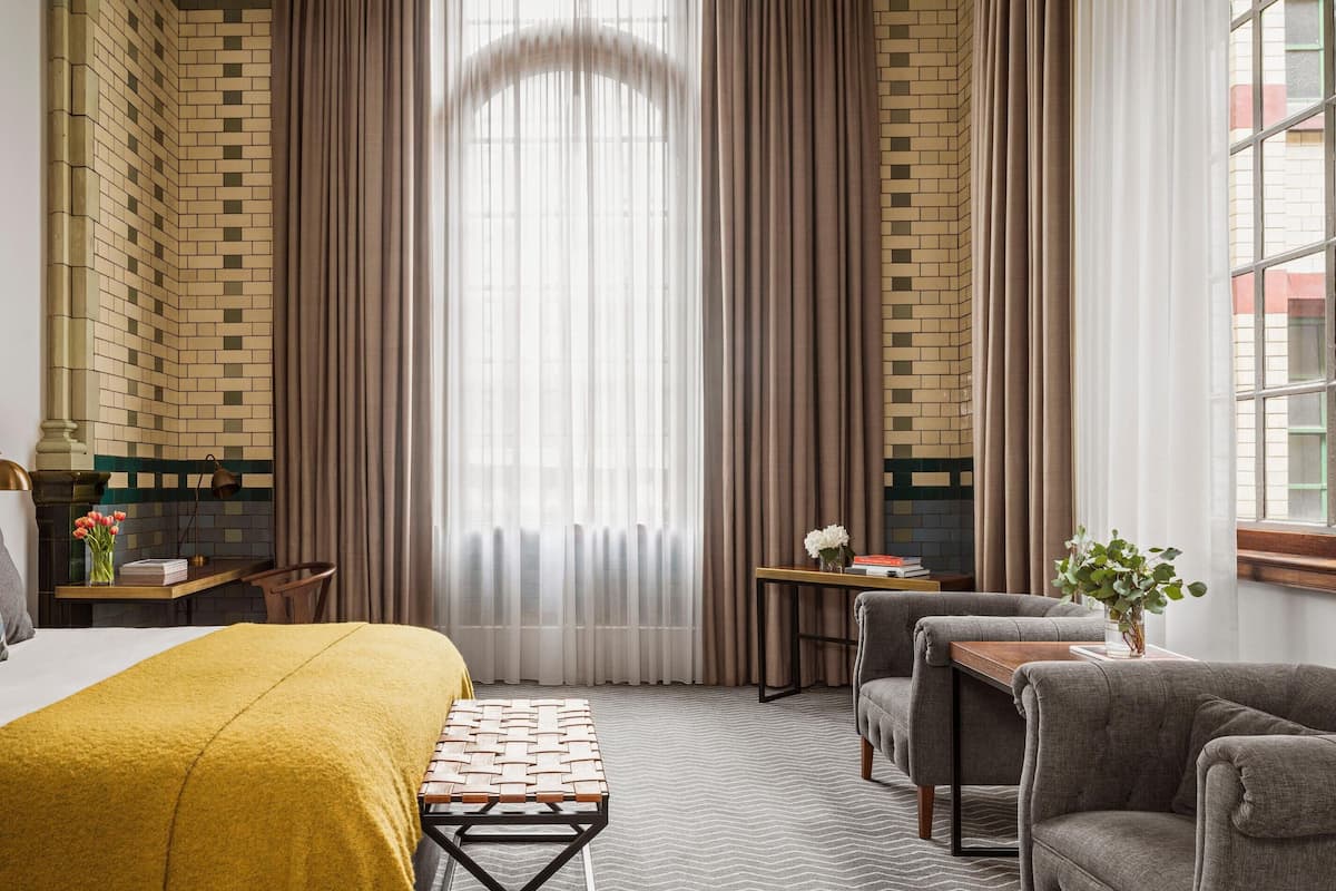 Une chambre d’hôtel avec un lit, un bureau, une chaise, un canapé et une fenêtre avec des rideaux.