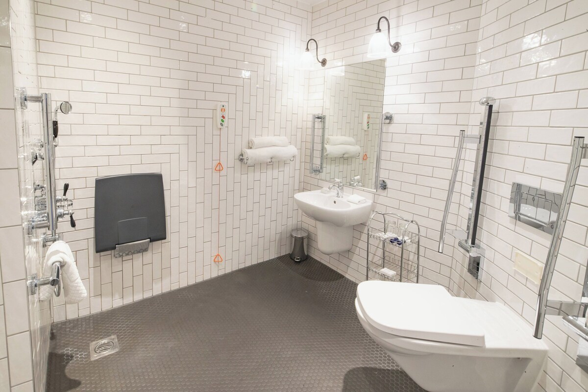 A modern bathroom with white tiled walls, a grey floor, a white sink, a toilet, and a shower area.