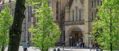A historic building with a prominent arched entrance and a sign reading "University of Manchester".