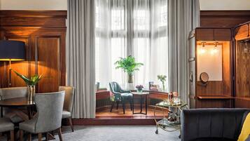 A hotel room with a dining area, a sofa, a cabinet, and a large window with curtains.