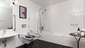 Un baño moderno con azulejos blancos tipo metro, piso hexagonal negro, ducha, lavamanos e inodoro con barra de apoyo.