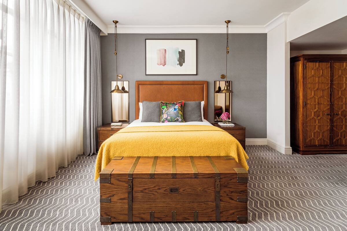 A hotel room with a large bed, a wooden chest, a nightstand, a lamp, and a wardrobe.