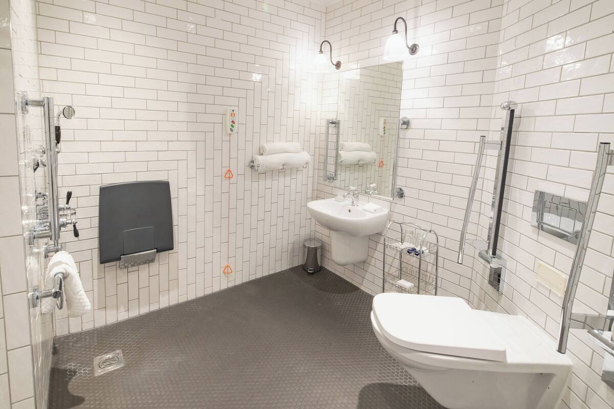 A modern bathroom with white tiled walls, a grey floor, a white sink, a toilet, and a shower area.