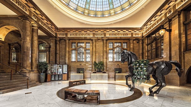 A grand lobby with a large horse statue, a central seating area, and a high ceiling with a skylight. - Kimpton Clocktower by IHG (Manchester)