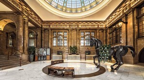 Un lobby espacioso con una gran estatua de un caballo, un área de estar central y un techo alto con tragaluces.