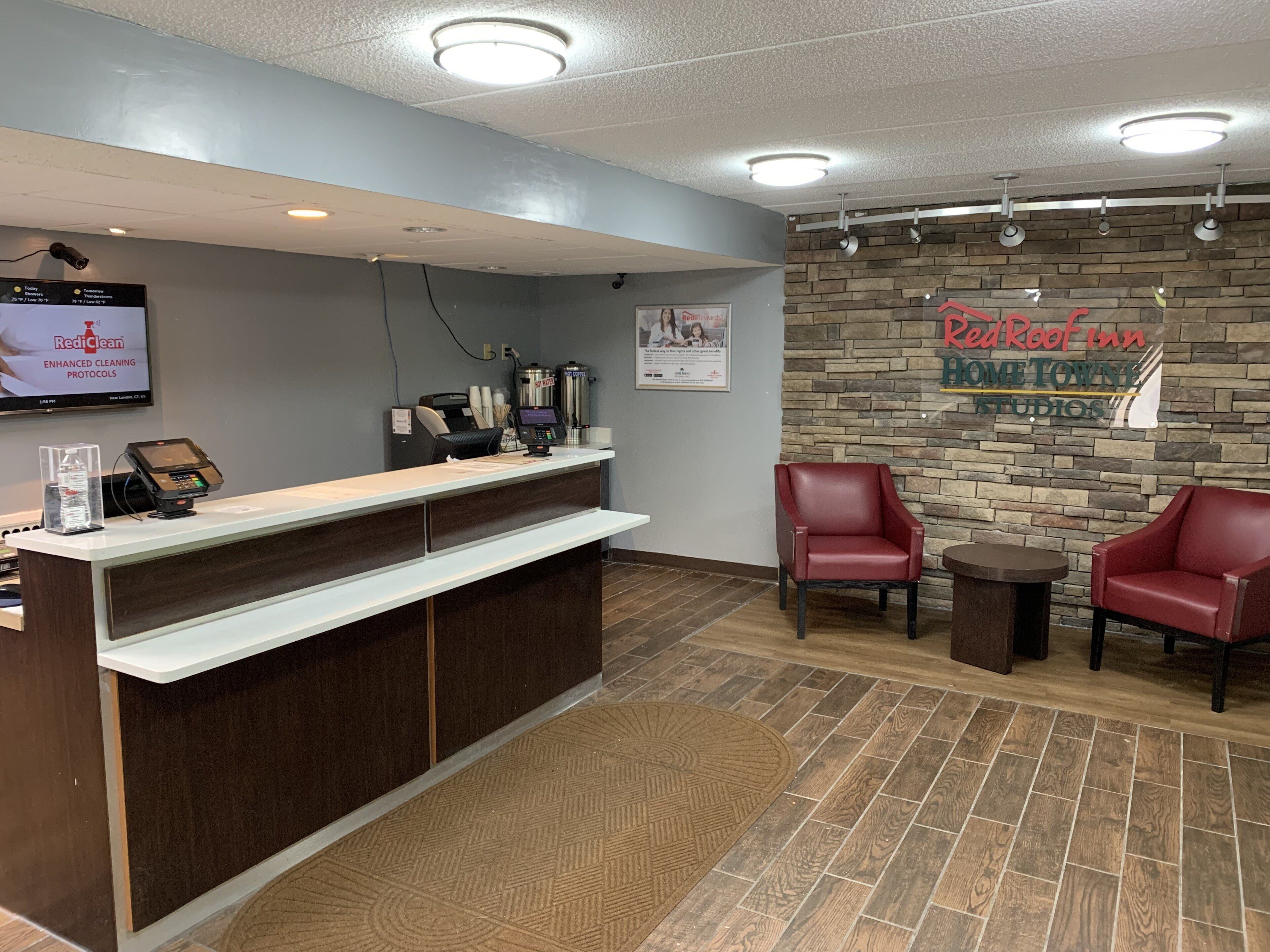 A reception area with a counter, a mounted television, a Red Roof Inn sign, and two red chairs.