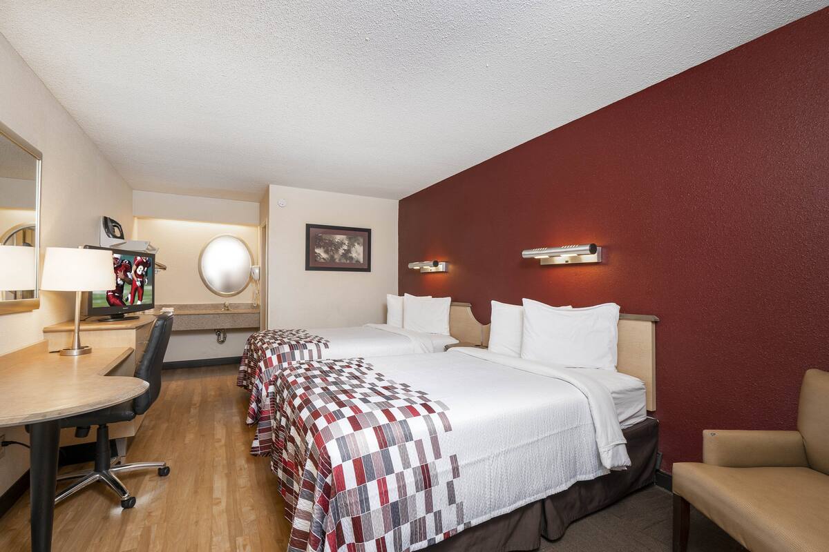 A hotel room with two beds, a desk, a chair, a TV, and a mirror.