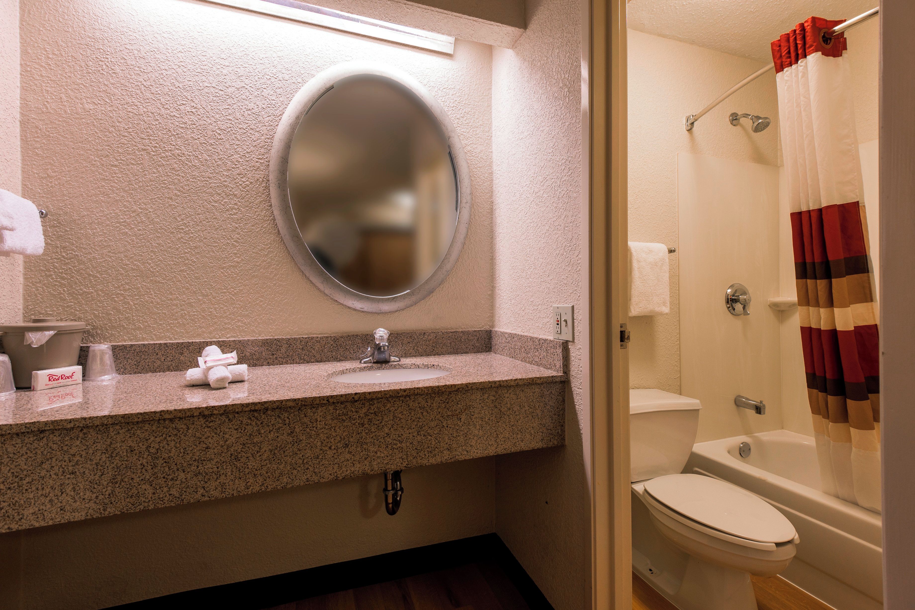 A bathroom with a granite countertop, a round mirror, a toilet, and a shower with a striped curtain.