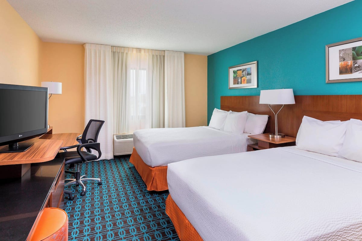 A hotel room with two beds, a desk with a computer, a TV, and a chair.