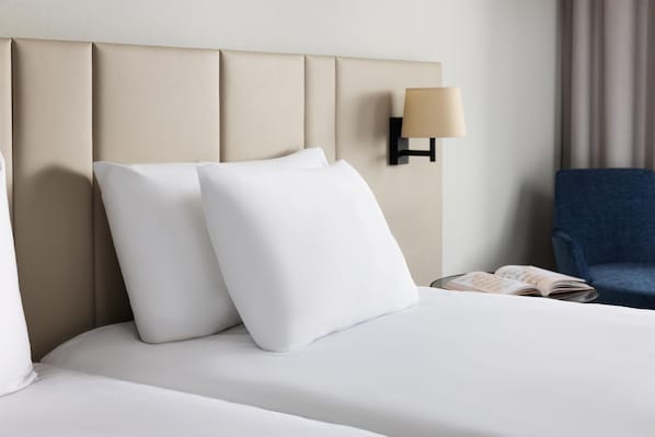 A hotel room with a bed, pillows, a lamp, a chair, and a book.