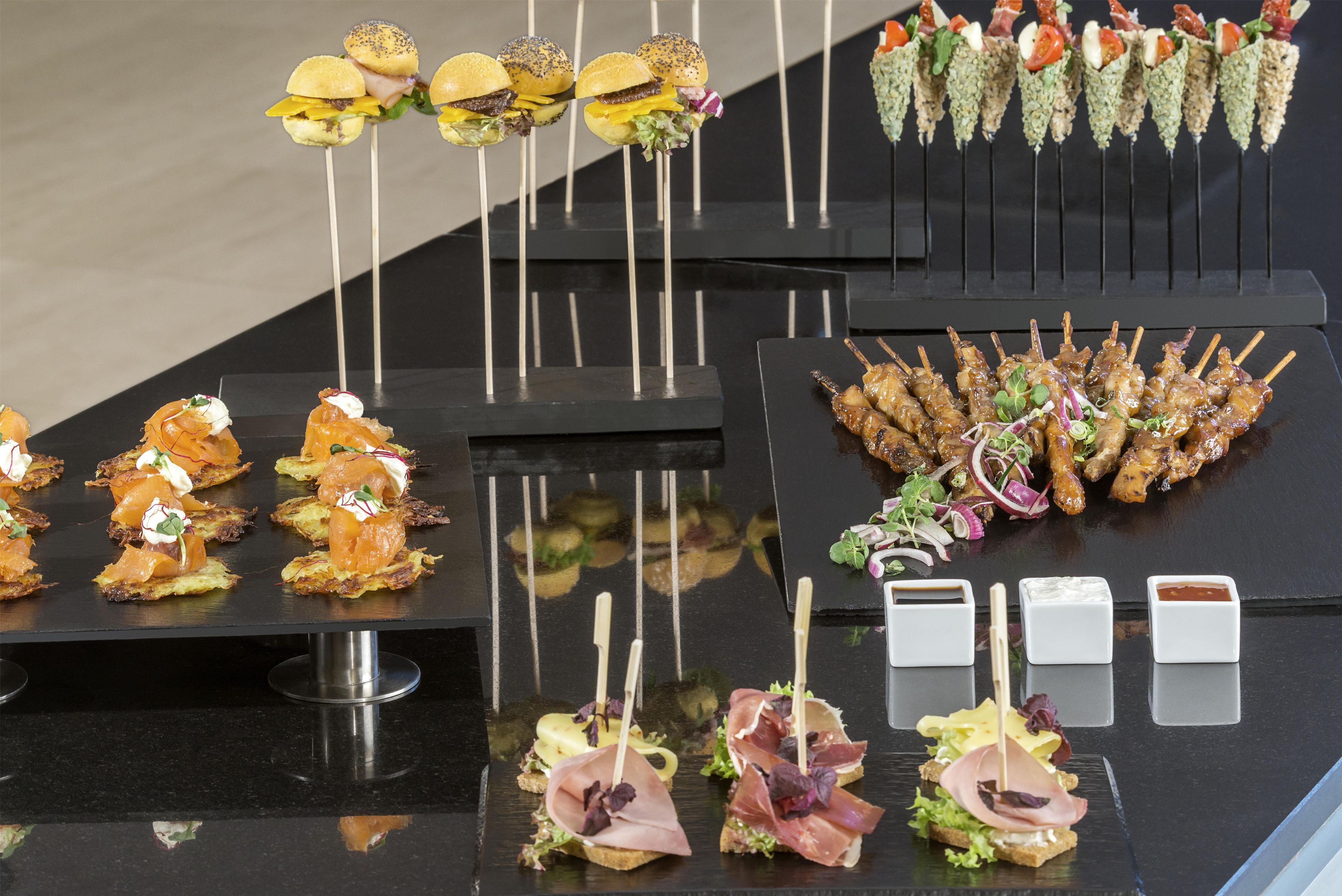 Diverse hapjes en gerechten gepresenteerd op een zwart dienblad, waaronder belegde broodjes, spiesjes en voorgerechten.