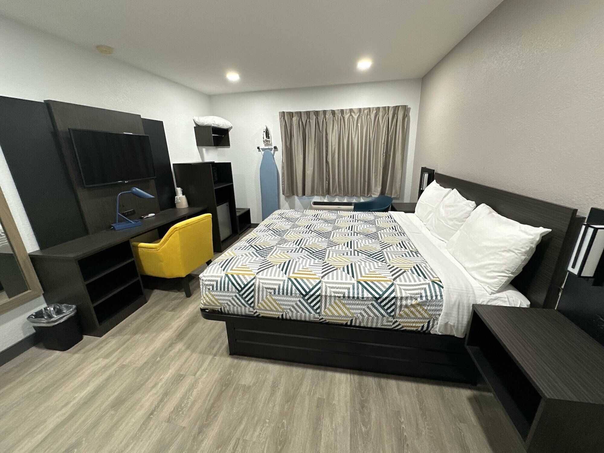A modern hotel room with a large bed, a desk with a chair, a television, and a window with curtains.