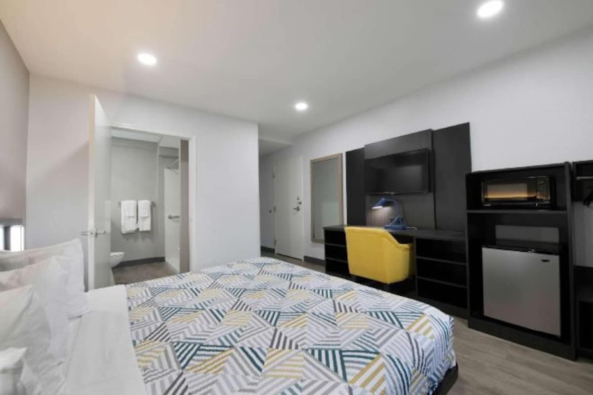 Ein modernes Hotelzimmer mit einem Bett, einem Fernseher, einer kleinen Kühlbox und einem gelben Sessel.