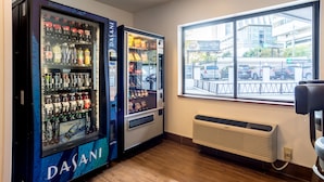 Une pièce équipée de deux distributeurs automatiques d’eau Dasani, d’une grande fenêtre donnant sur un parking et des immeubles, et d’un climatiseur fixé au mur.