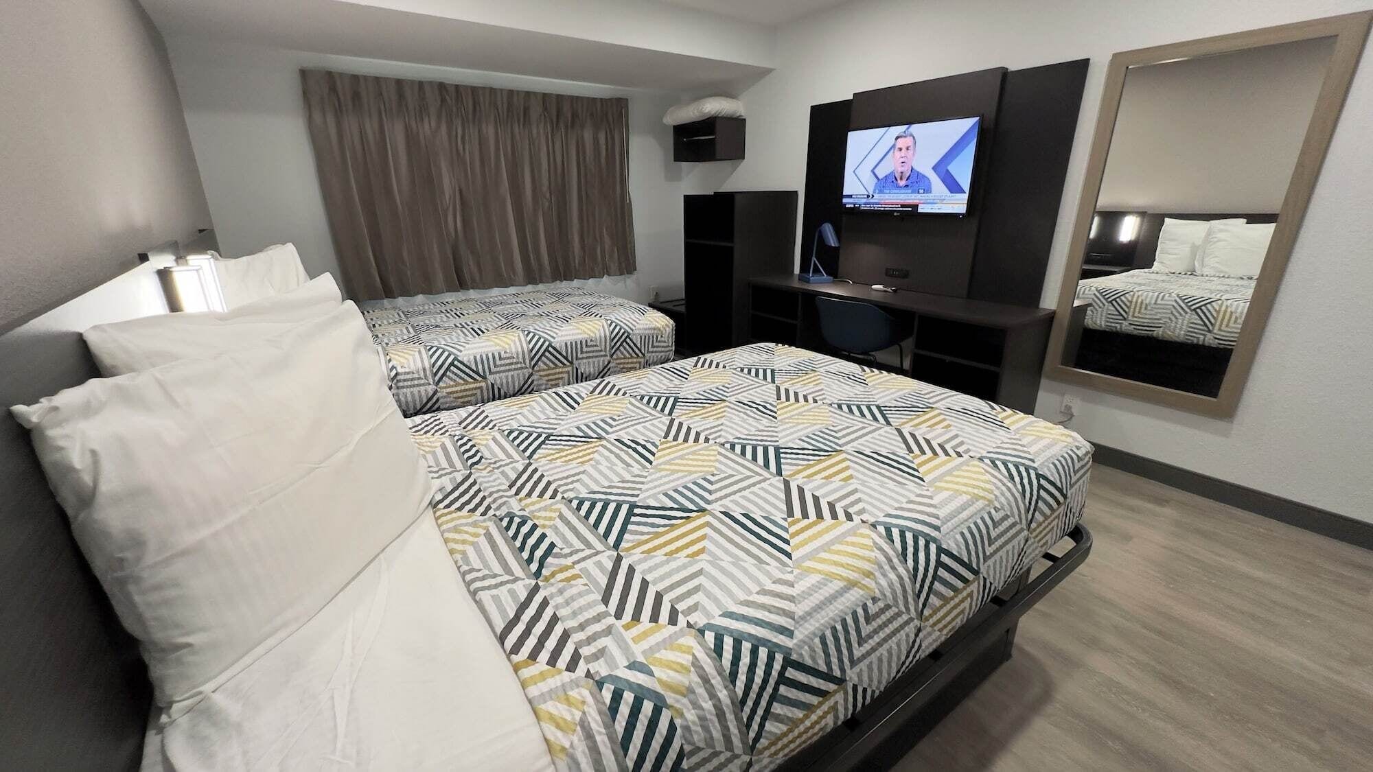 A hotel room with two beds, a desk, a television, and a mirror.