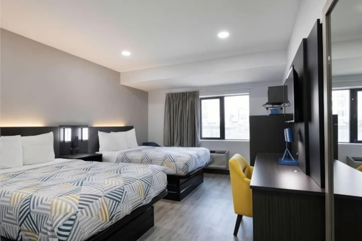 Ein Hotelzimmer mit zwei Betten, einem Schreibtisch, einem Stuhl, einem Fernseher und einem Fenster mit Vorhängen.