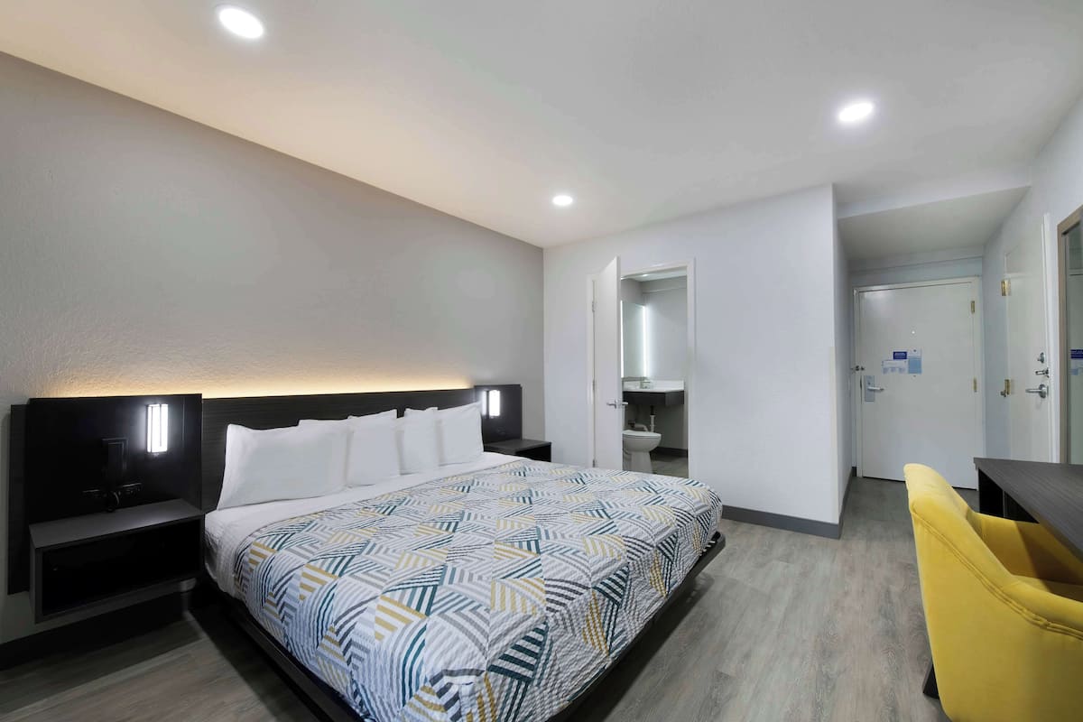 Habitación de hotel con una cama grande, mesitas de noche, un escritorio, una silla y un baño visible a través de una puerta abierta.