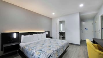 A hotel room with a large bed, bedside tables, a desk, a chair, and a bathroom visible through an open door.