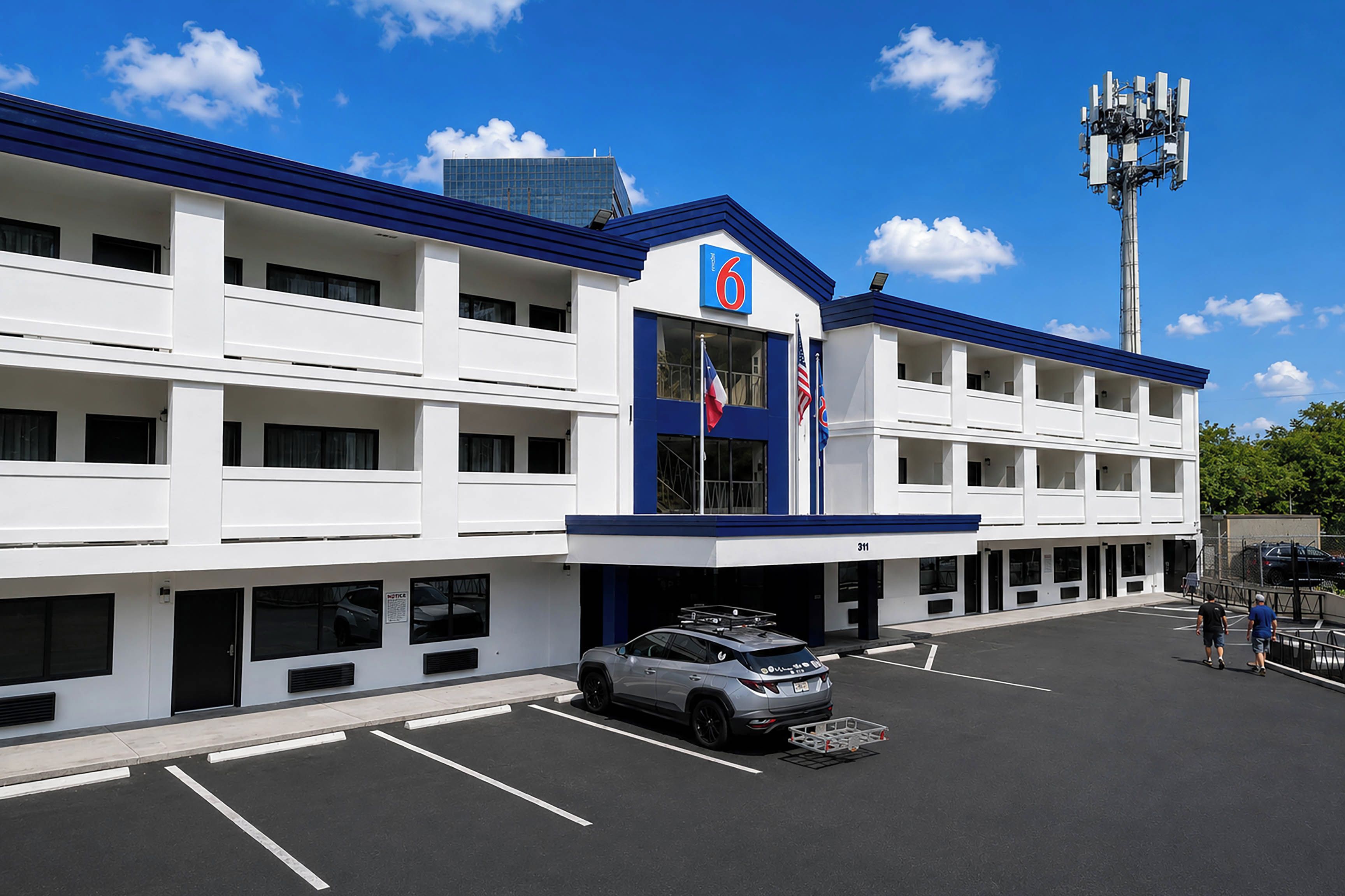Een meerlaags hotel met een blauw-witte gevel, een parkeerplaats en een vlaggenmast met vlaggen.
