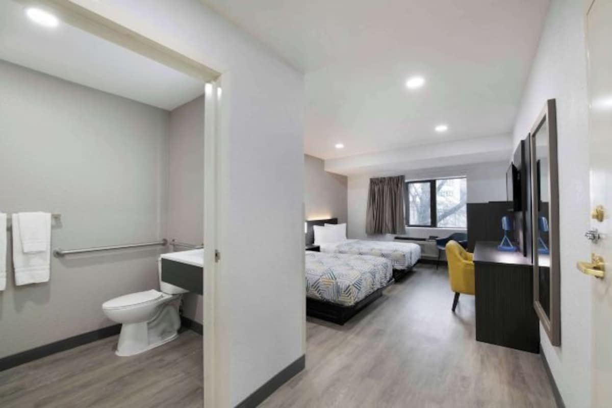 Ein modernes Hotelzimmer mit Bad, zwei Betten, einem Schreibtisch und einem Sessel.