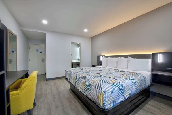 A modern hotel room with a large bed, a desk, a chair, and a mirror.