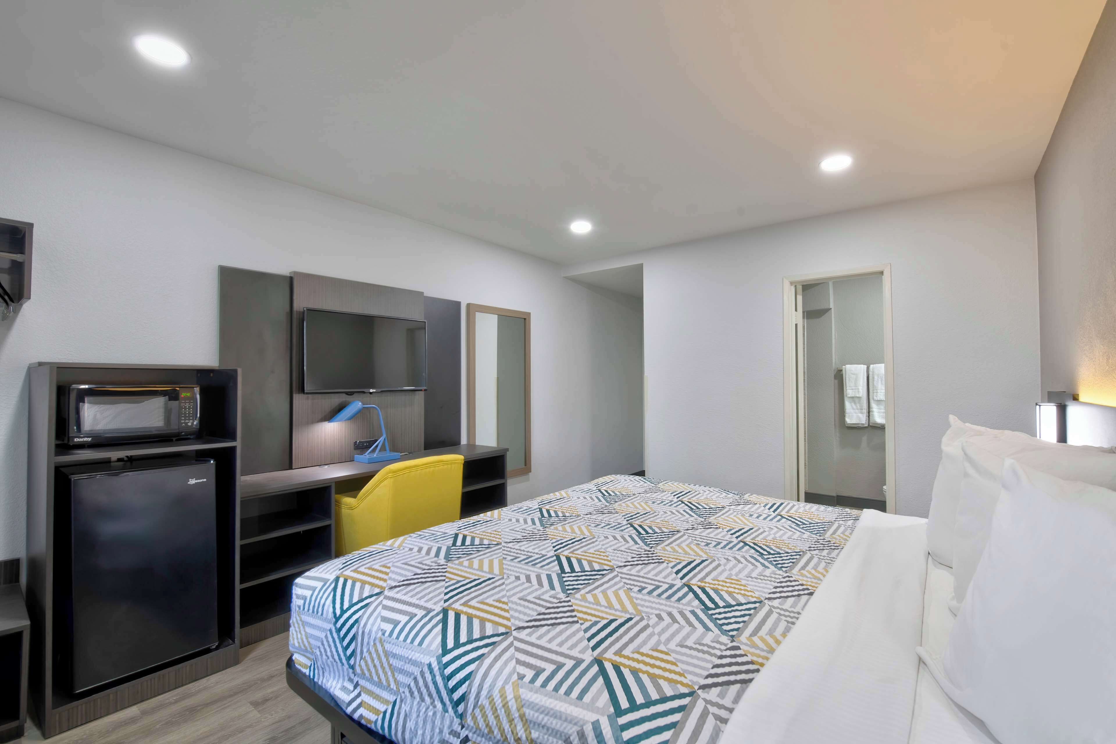 A hotel room with a bed, a desk with a computer, a microwave, and a refrigerator.