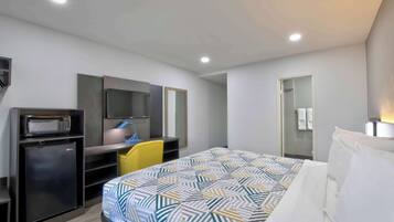 A hotel room with a bed, a desk with a computer, a microwave, and a refrigerator.