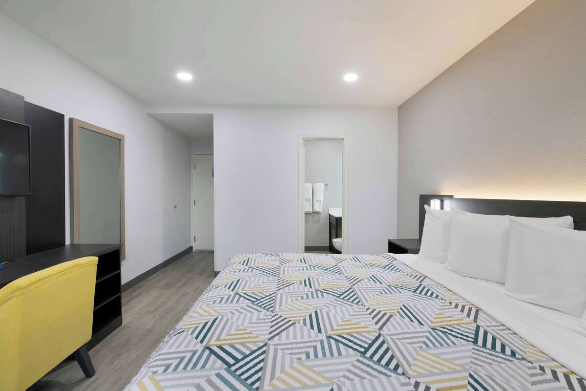 Una habitación de hotel con cama, escritorio, silla y espejo.