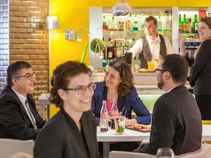 A restaurant with a brick wall, a bar area with bottles, and a group of people dining. - Mercure Paris Massy Gare TGV (Massy)