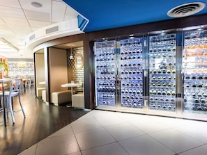 A hotel lobby with a wine cooler, seating area, and a view of the restaurant. - Mercure Paris Massy Gare TGV (Massy)