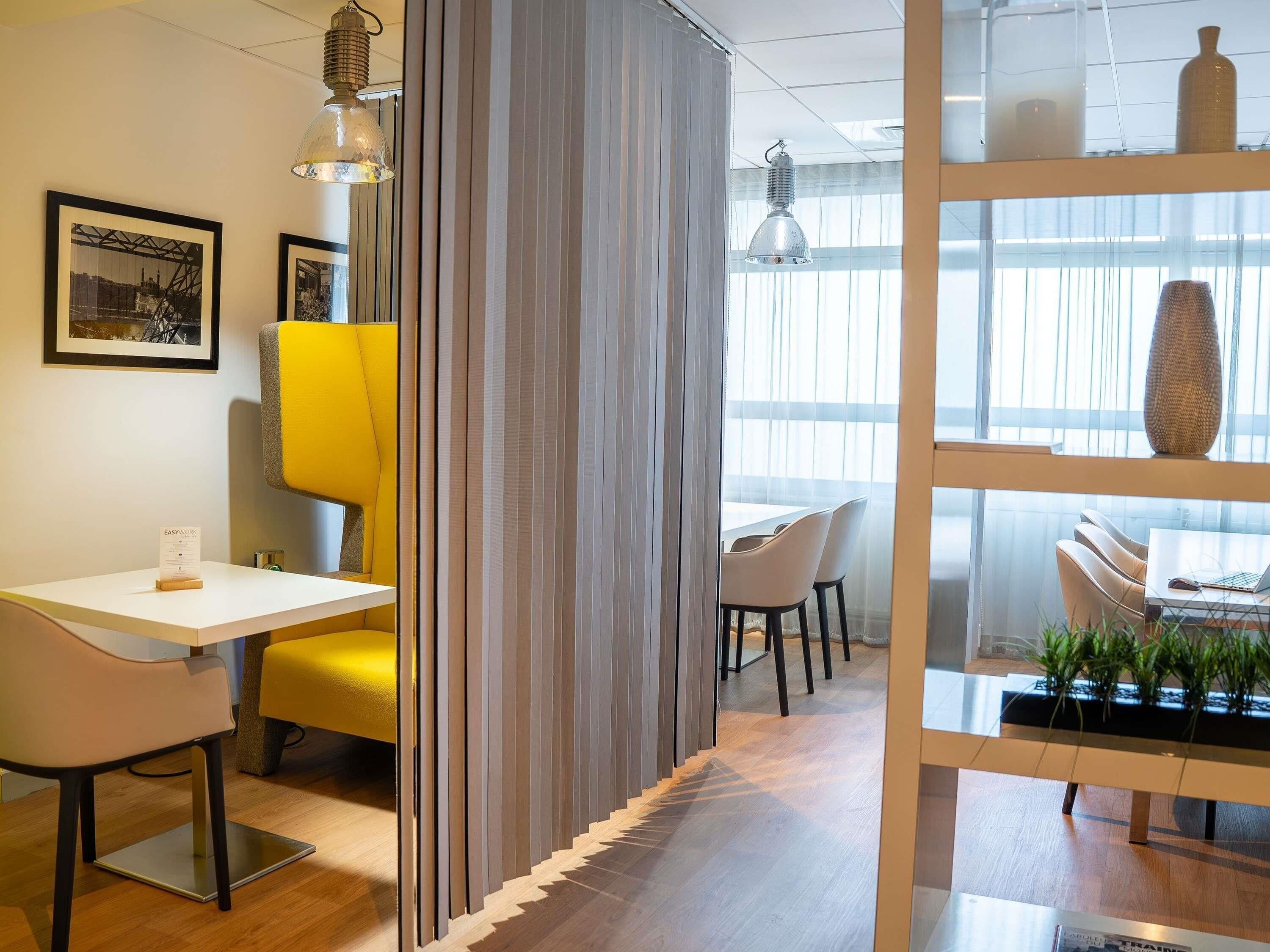 A modern office space with a desk, chairs, a glass partition, and a view of the outdoors.