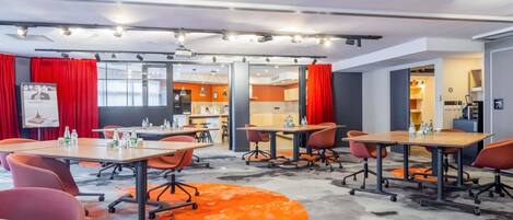 A modern conference room with tables, chairs, and a kitchen area visible through an open door.