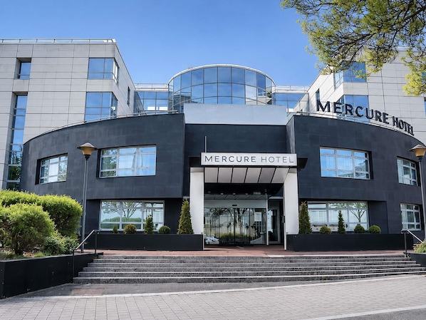 Un hĂŽtel moderne Ă la façade incurvĂ©e, dotĂ© de grandes fenĂȘtres et dâune entrĂ©e imposante.