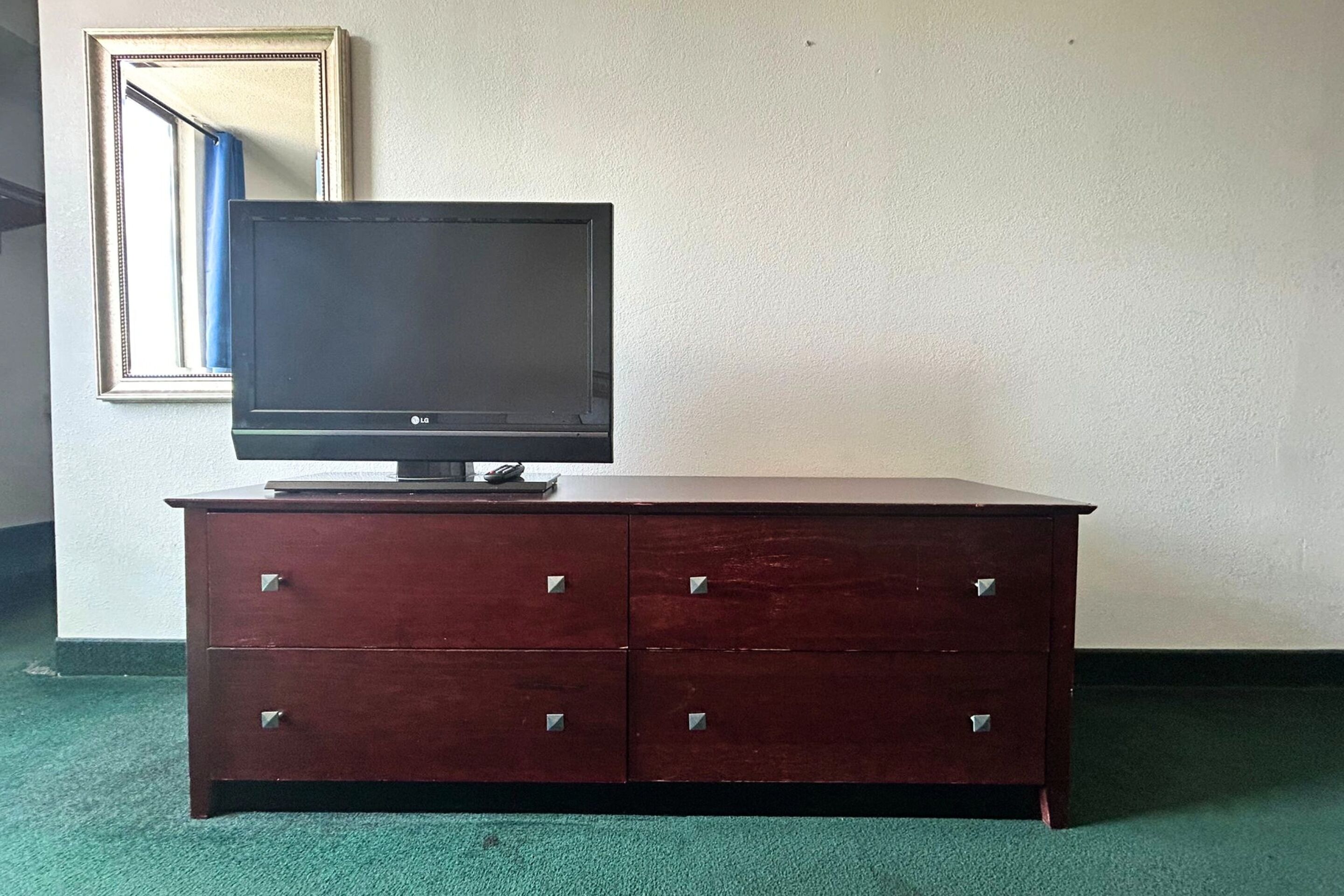 Un aparador de madera con un televisor de pantalla plana encima, frente a una pared lisa con un espejo.
