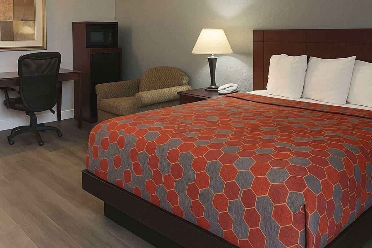 A hotel room with a bed, a desk, a chair, a lamp, and a television.
