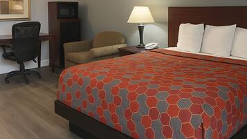 A hotel room with a bed, a desk, a chair, a lamp, and a television.