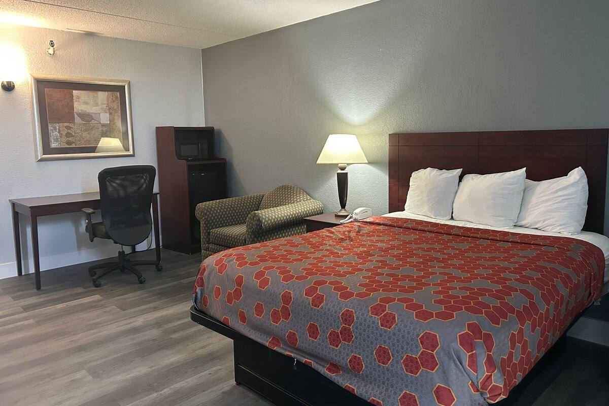 A hotel room with a bed, desk, chair, TV, and lamp.