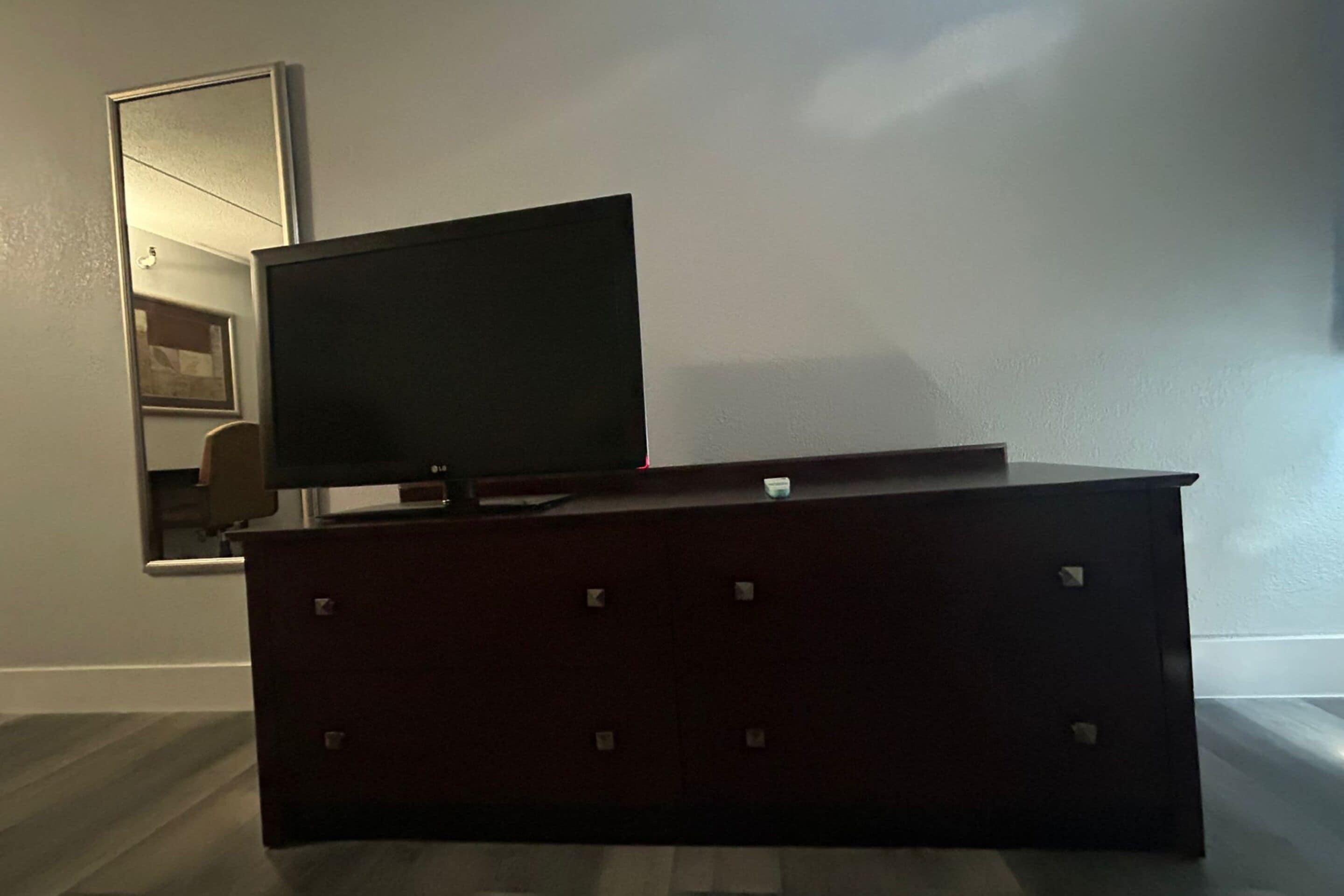 Un aparador de madera oscura con un televisor de pantalla plana encima, ubicado frente a una pared lisa con una puerta y un espejo.