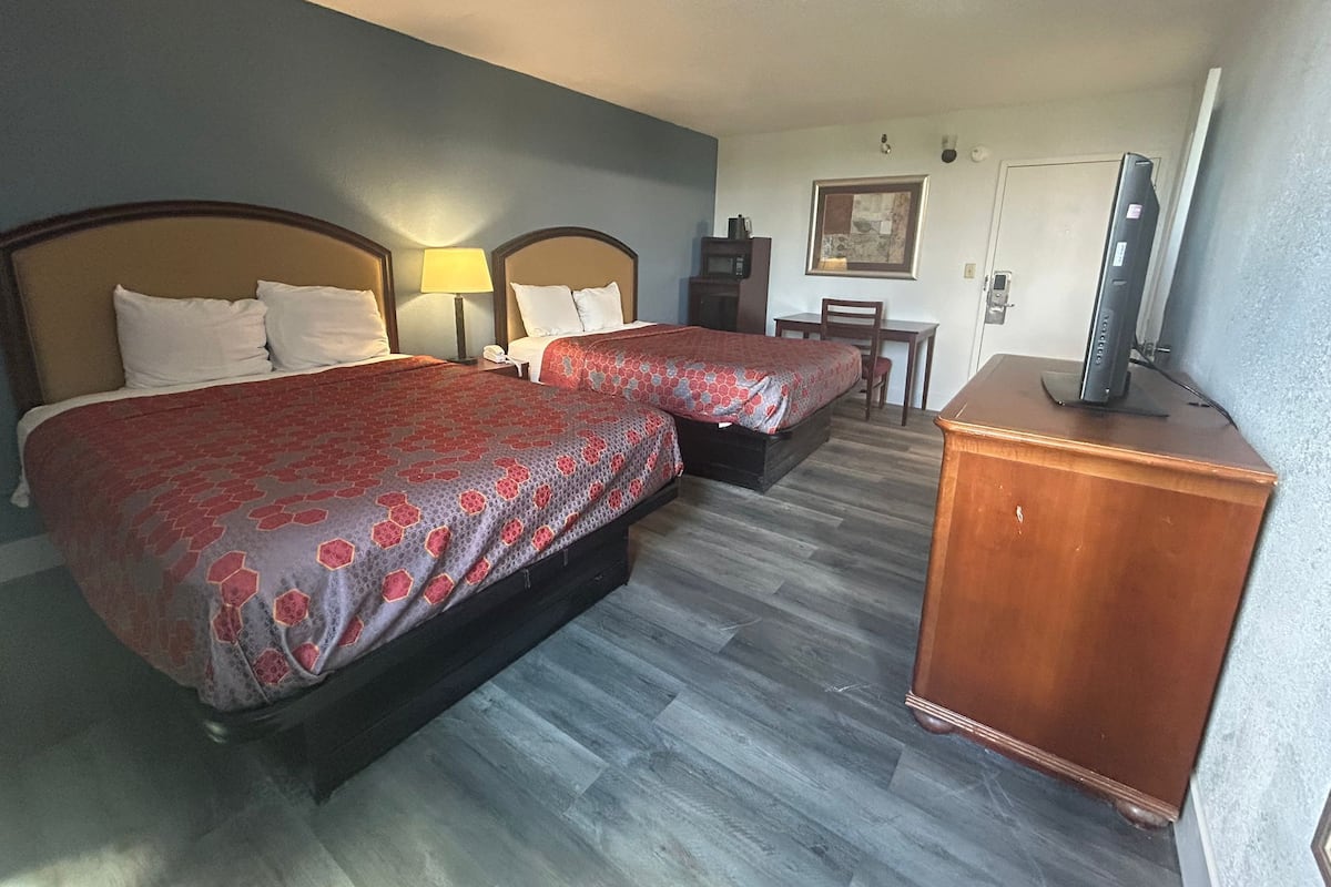 A hotel room with two beds, a desk, a chair, a television, and a microwave.