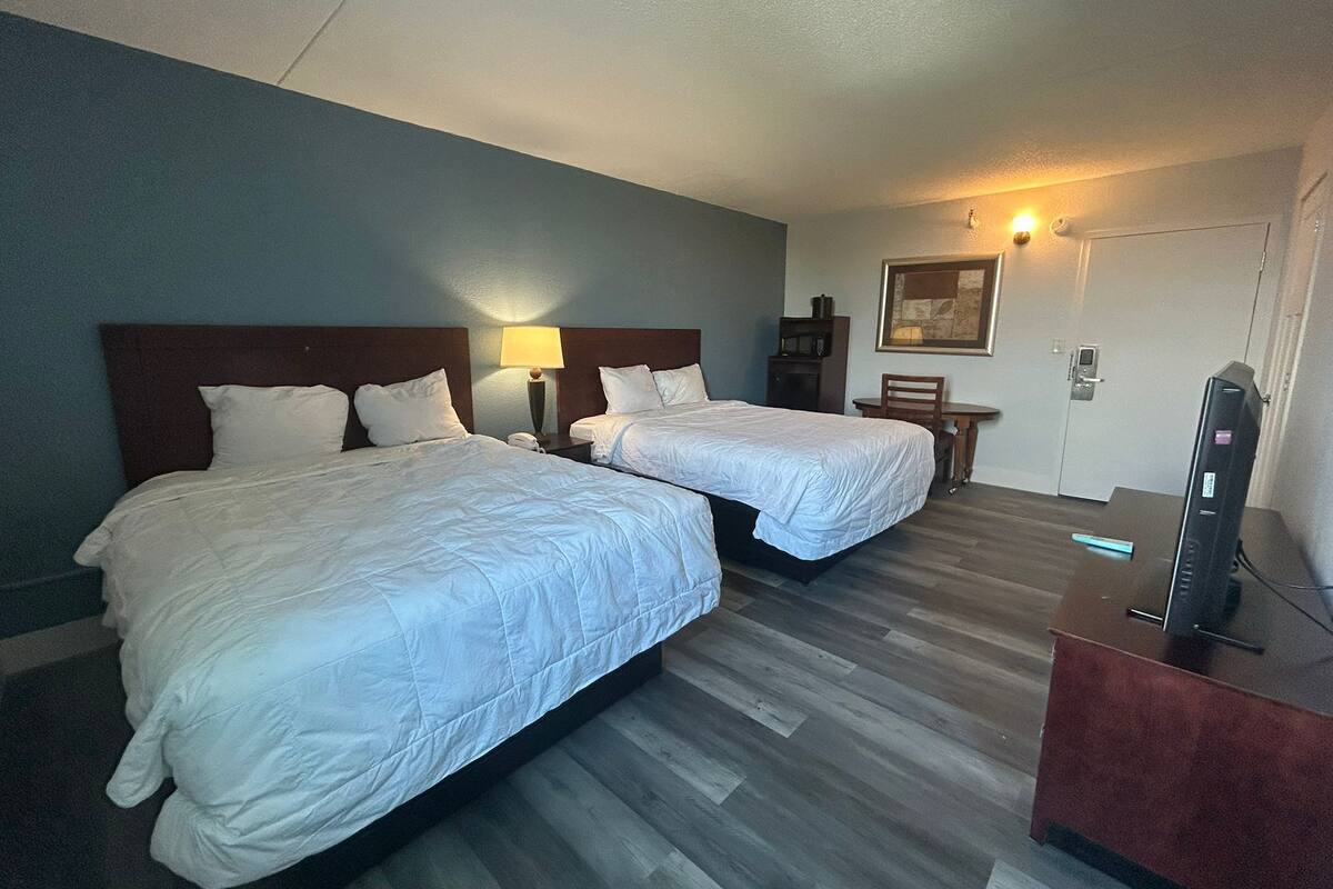 A hotel room with two beds, a desk, a chair, a TV, and a door.