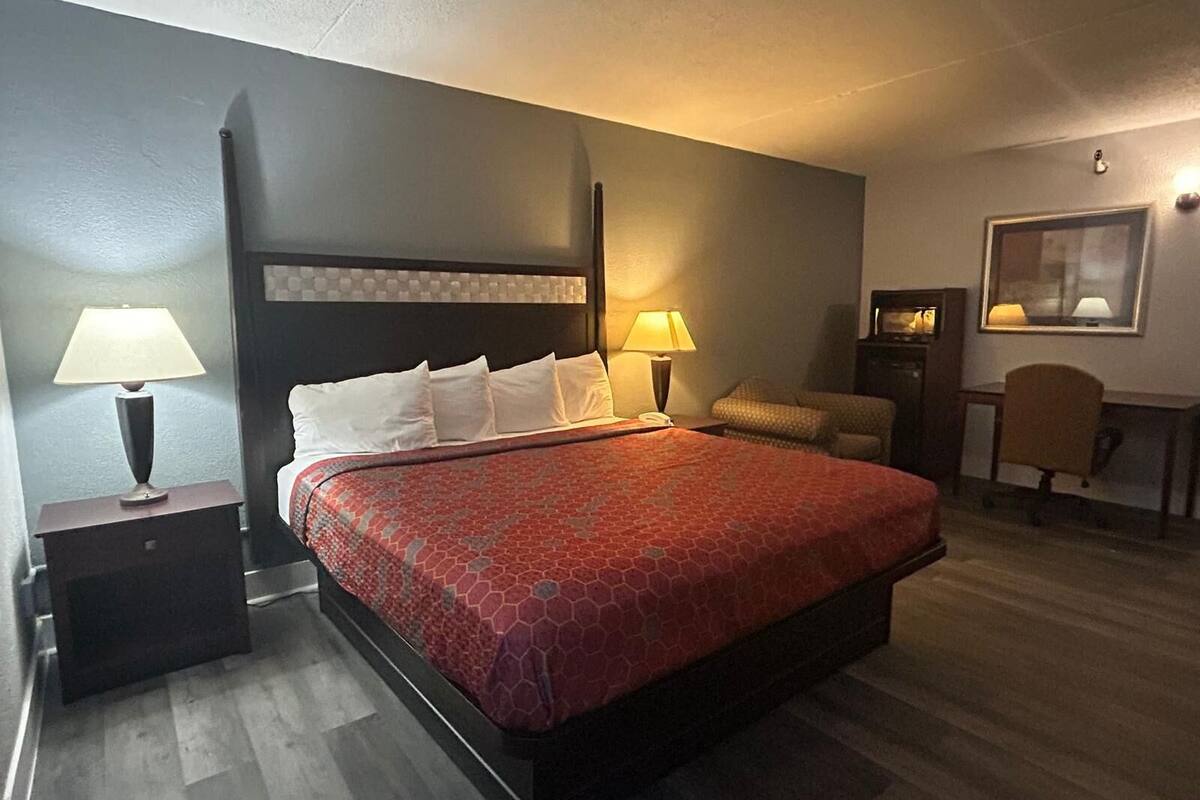 A hotel room with a bed, two bedside tables, a desk, a chair, and a lamp.